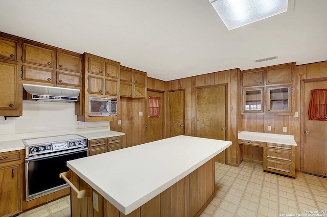 1212 County Road 337, La Vernia, TX 78121 - kitchen with range with electric cooktop, under cabinet range hood, built in microwave, brown cabinets, and wood walls