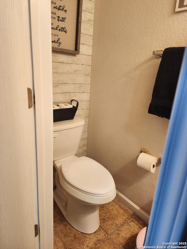 510 Tres Caminos, San Antonio, TX 78245 - bathroom with toilet, tile patterned flooring, wooden walls, baseboards, and a textured wall