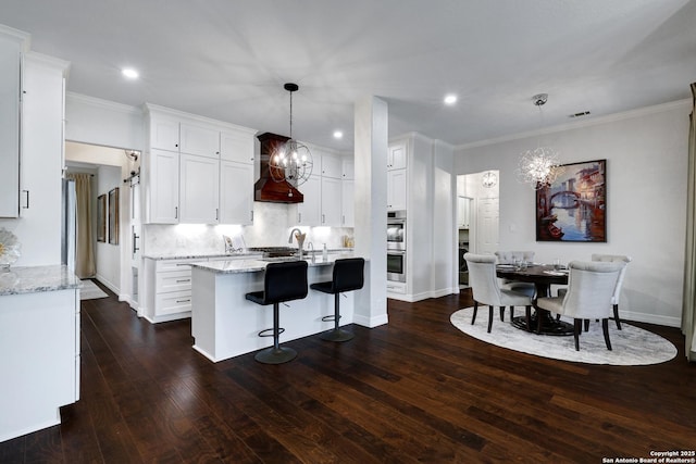 11 Gemsbuck Rise, San Antonio, TX 78258 - kitchen with a chandelier, premium range hood, white cabinetry, crown molding, and dark wood-style flooring