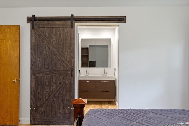 305 Rockmoor Dr, Georgetown, TX 78628 - bedroom featuring a barn door, wood finished floors, a sink, and ensuite bath