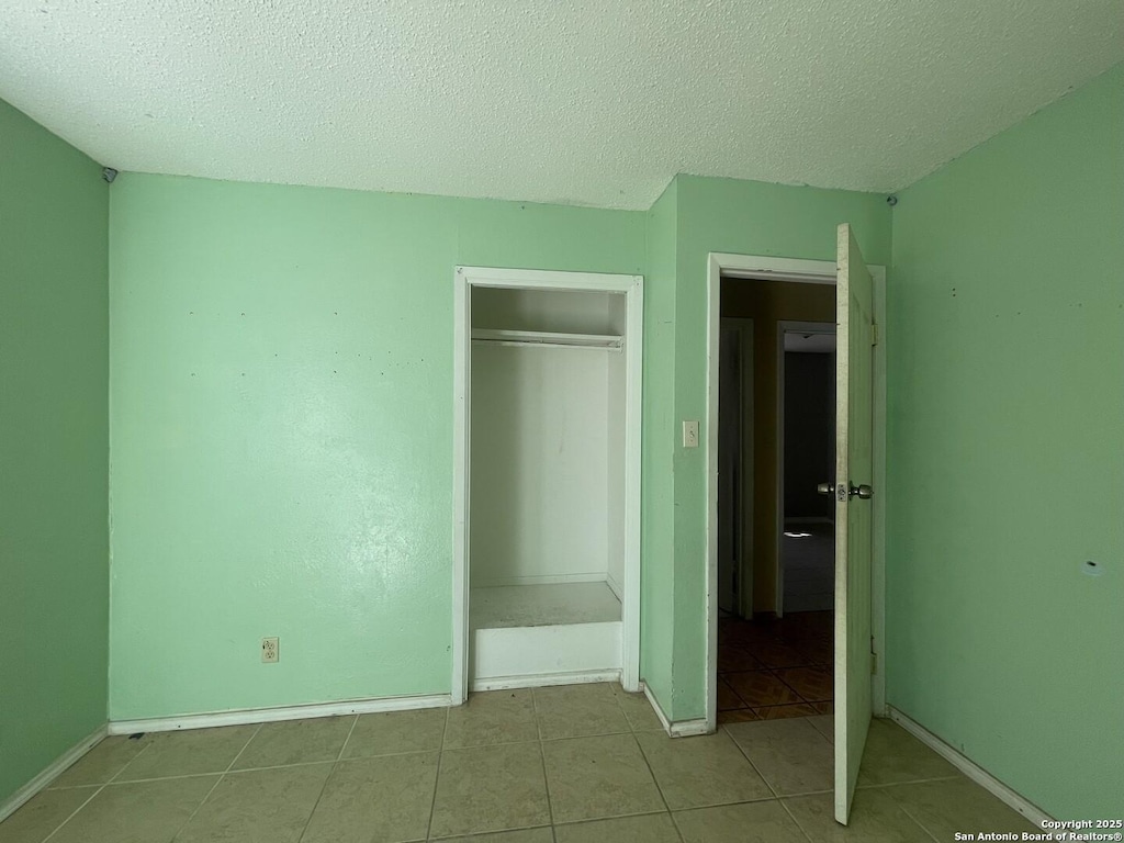 4402 Dove Spgs, Austin, TX 78744 - unfurnished bedroom featuring a closet, tile patterned flooring, baseboards, and a textured ceiling