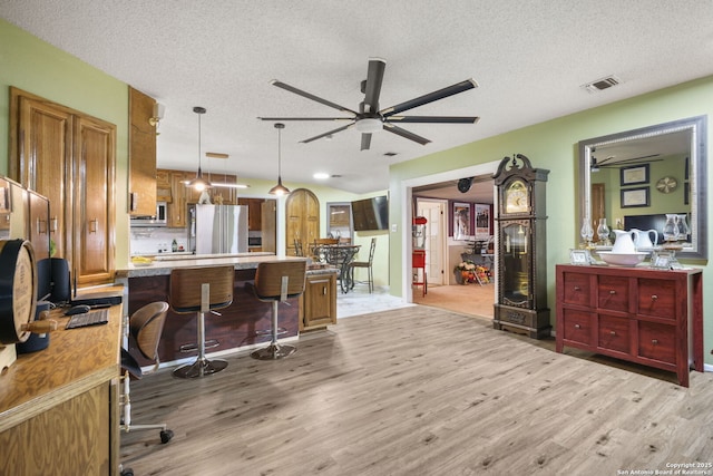 102 Southgate, Pleasanton, TX 78064 - kitchen with freestanding refrigerator, ceiling fan, light wood-type flooring, brown cabinetry, and a textured ceiling