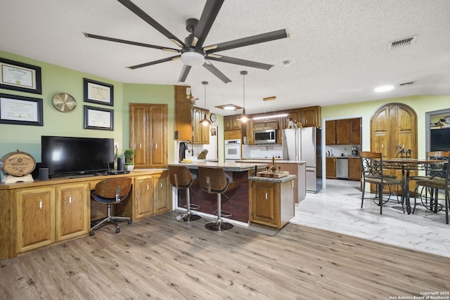102 Southgate, Pleasanton, TX 78064 - kitchen with appliances with stainless steel finishes, a peninsula, a ceiling fan, light wood-type flooring, and a textured ceiling