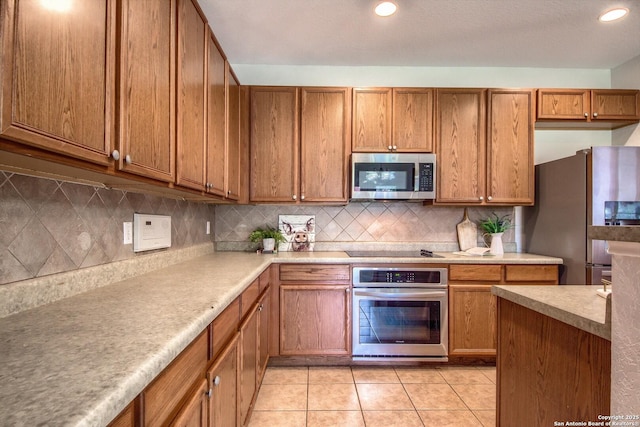 112 Springtree Bnd, Cibolo, TX 78108 - kitchen with stainless steel appliances, brown cabinetry, light tile patterned flooring, backsplash, and light countertops