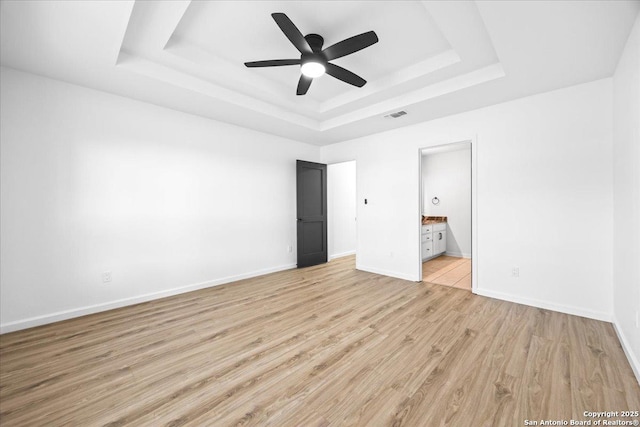268 Cordova Loop, Seguin, TX 78155 - unfurnished bedroom with a tray ceiling, light wood finished floors, baseboards, and ensuite bathroom