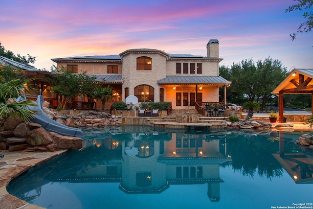 16227 San Cayetano, Helotes, TX 78023 - back of property at dusk with a standing seam roof, a patio area, roof mounted solar panels, a chimney, and an outdoor pool