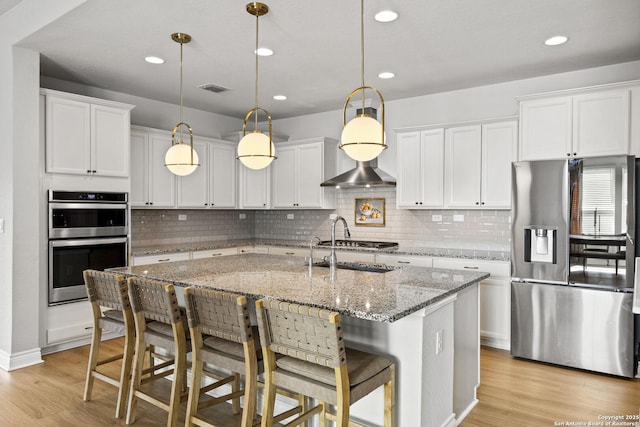 7618 Desperado, Boerne, TX 78015 - kitchen with stainless steel appliances, light wood-style floors, a kitchen island with sink, backsplash, and a kitchen bar