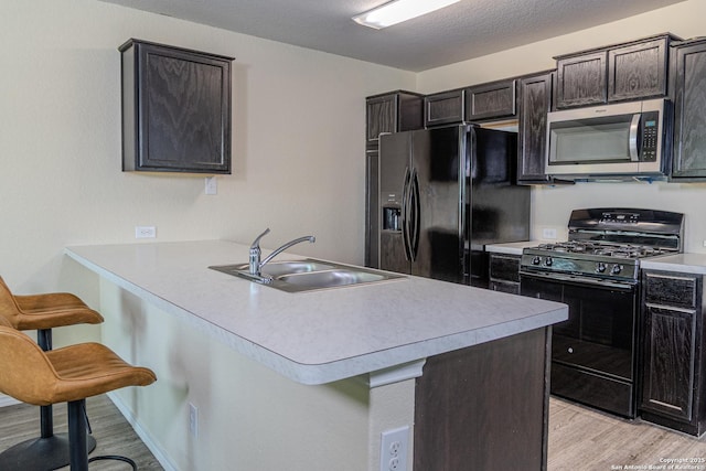5922 Autumn Palms, San Antonio, TX 78242 - kitchen with black appliances, a sink, light wood-style floors, a breakfast bar, and light countertops