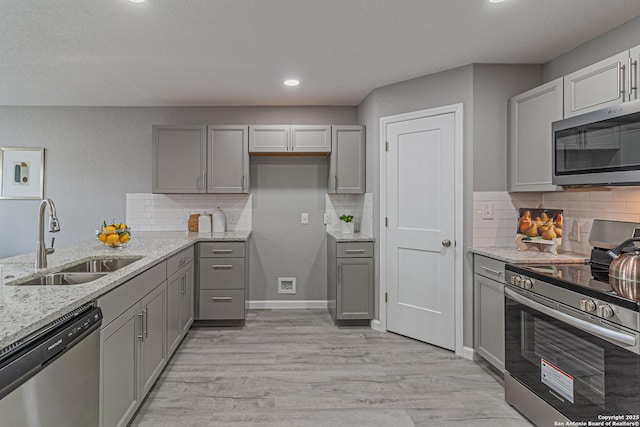 4935 Bartmer Ave, San Antonio, TX 78228 - kitchen with appliances with stainless steel finishes, gray cabinetry, light wood-style flooring, light stone countertops, and backsplash