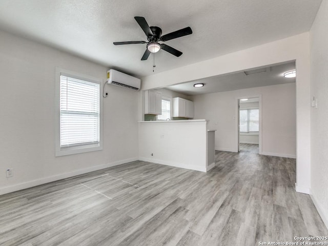 815 Flanders, San Antonio, TX 78211 - unfurnished living room featuring a wall mounted AC, light wood finished floors, a ceiling fan, and healthy amount of natural light