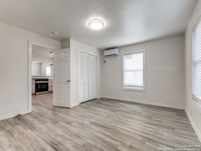 815 Flanders, San Antonio, TX 78211 - unfurnished bedroom featuring a wall unit AC, light wood-style floors, baseboards, multiple windows, and a textured ceiling