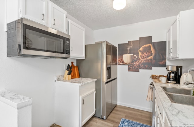 9630 NW Simplicity Dr, San Antonio, TX 78245 - kitchen featuring stainless steel appliances, a sink, light wood-style floors, white cabinetry, and light countertops