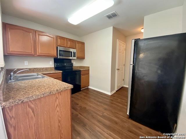 6926 Lunar Way, San Antonio, TX 78109 - kitchen with stainless steel microwave, black range with electric stovetop, freestanding refrigerator, a sink, and dark wood-type flooring