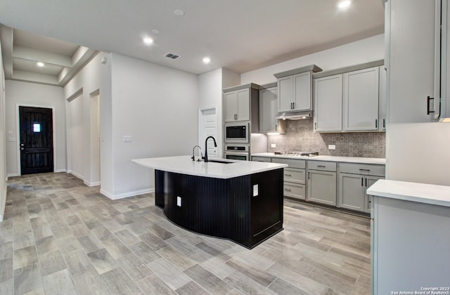 2035 Stephanie Ave, New Braunfels, TX 78132 - kitchen featuring backsplash, gray cabinets, light countertops, a sink, and a kitchen island with sink