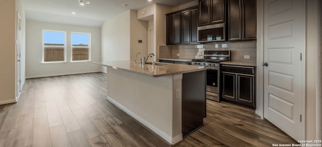 4506 Wild Goose, San Antonio, TX 78245 - kitchen featuring stainless steel appliances, dark wood finished floors, baseboards, tasteful backsplash, and an island with sink