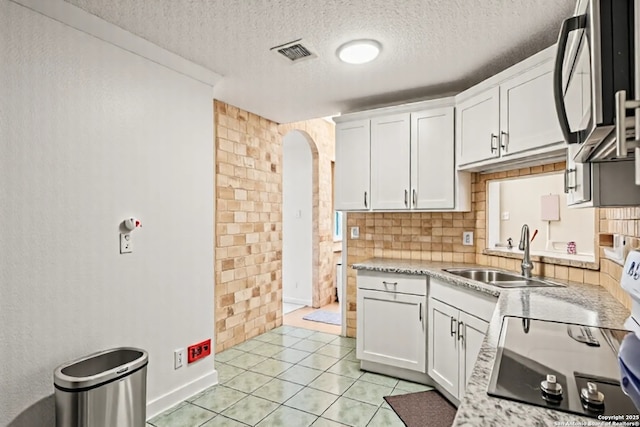 9927 Sandy Fld, San Antonio, TX 78245 - kitchen with arched walkways, a sink, a textured ceiling, white cabinetry, and tasteful backsplash