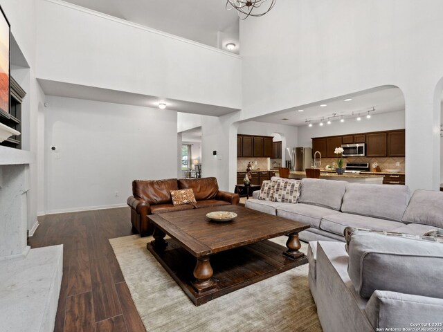 627 Midway, San Antonio, TX 78258 - living area featuring dark wood-type flooring, arched walkways, a towering ceiling, baseboards, and track lighting