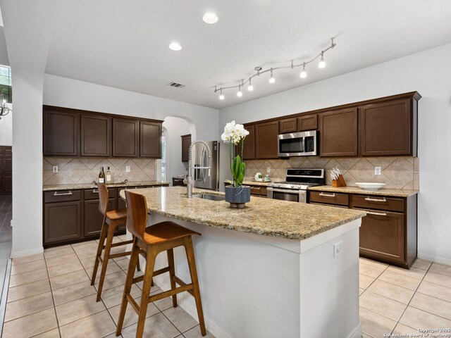 627 Midway, San Antonio, TX 78258 - kitchen with stainless steel appliances, arched walkways, light tile patterned flooring, backsplash, and a kitchen island with sink