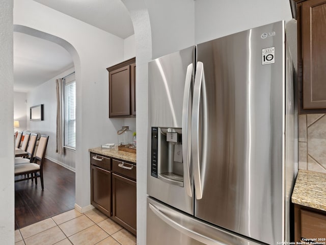 627 Midway, San Antonio, TX 78258 - kitchen with stainless steel fridge with ice dispenser, arched walkways, light stone countertops, light tile patterned floors, and dark brown cabinets