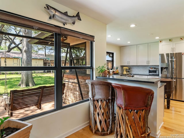 134 Camellia Way, San Antonio, TX 78209 - kitchen featuring stainless steel refrigerator with ice dispenser, light wood-type flooring, dark countertops, white cabinets, and tasteful backsplash