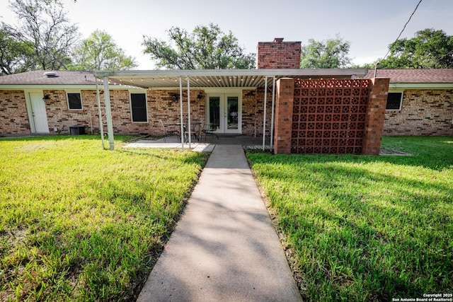 902 Newhall, Beeville, TX 78102 - view of front of house featuring french doors, a chimney, a front lawn, a patio, and brick siding