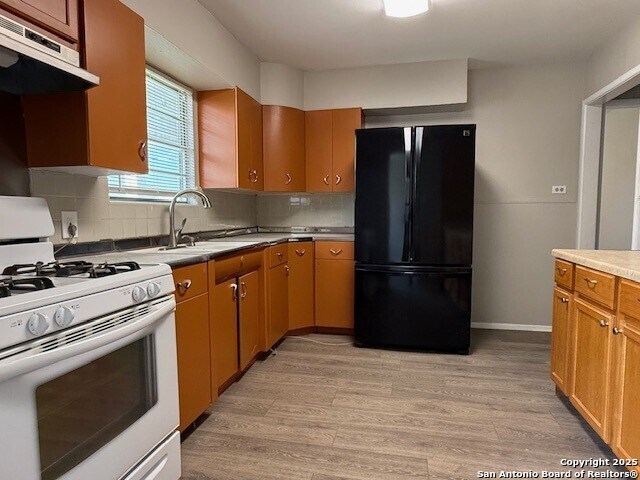 130 Nedrub Dr, San Antonio, TX 78223 - kitchen featuring white gas range, freestanding refrigerator, ventilation hood, light wood-style floors, and decorative backsplash