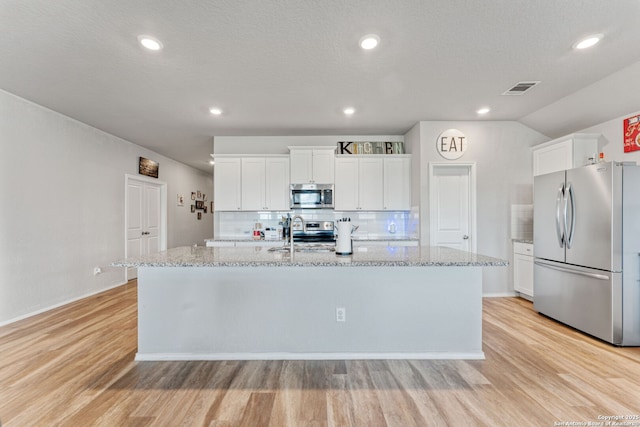 2946 Daisy Mdw, New Braunfels, TX 78130 - kitchen featuring stainless steel appliances, light wood-style floors, an island with sink, white cabinets, and light stone counters