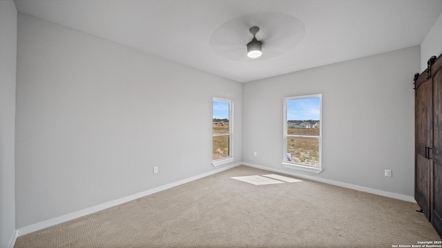 201 Lakeview Cir, La Vernia, TX 78121 - unfurnished bedroom with a barn door, carpet flooring, baseboards, and a ceiling fan