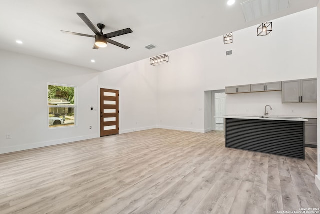 259 Future, San Antonio, TX 78213 - unfurnished living room with light wood-style flooring, ceiling fan, baseboards, a sink, and a towering ceiling