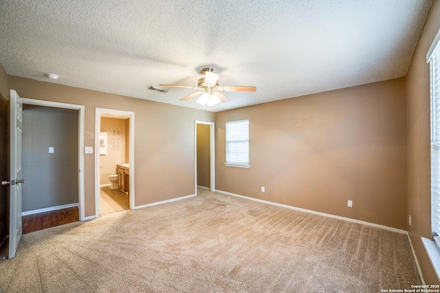 756 County Road 245, Hondo, TX 78861 - unfurnished bedroom featuring light carpet, baseboards, ensuite bath, a textured ceiling, and a ceiling fan