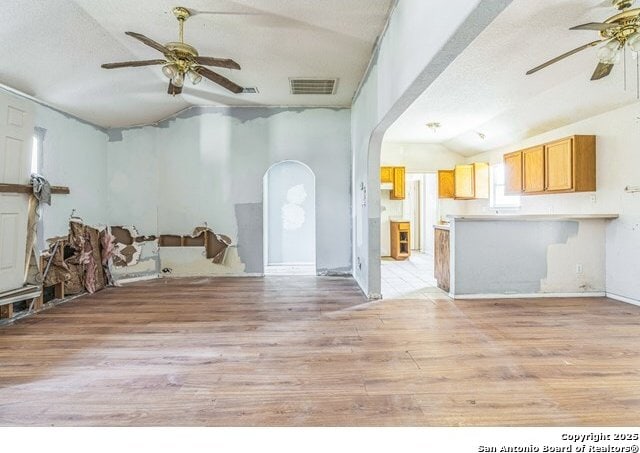 2514 Christian, San Antonio, TX 78222 - unfurnished living room featuring a ceiling fan, vaulted ceiling, light wood finished floors, arched walkways, and a textured ceiling