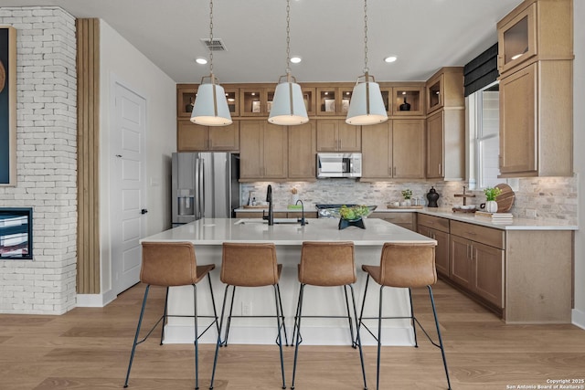 20675 Huebner Rd, San Antonio, TX 78258 - kitchen with appliances with stainless steel finishes, tasteful backsplash, a breakfast bar area, brown cabinetry, and a kitchen island with sink