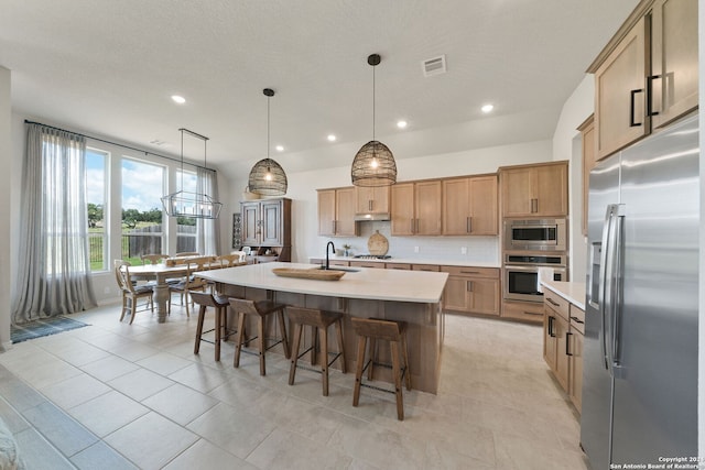 122 Indigo Bnd, Boerne, TX 78006 - kitchen with stainless steel appliances, light countertops, decorative backsplash, a kitchen breakfast bar, and a kitchen island with sink