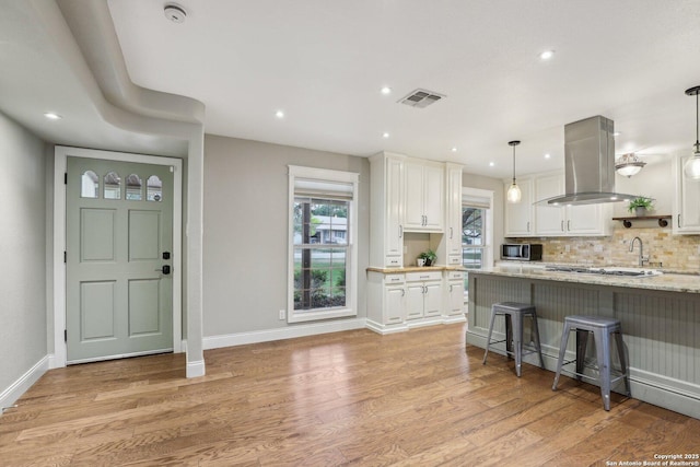 12102 Cherry Blossom, San Antonio, TX 78247 - kitchen featuring island exhaust hood, white cabinets, light wood-style flooring, light stone countertops, and a kitchen breakfast bar