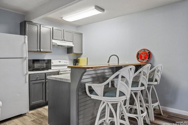 1215 Amanda, Canyon Lake, TX 78133 - kitchen with white appliances, gray cabinetry, under cabinet range hood, a breakfast bar, and light wood-style floors