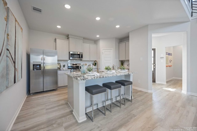 11212 Schmidt Ln, Converse, TX 78109 - kitchen featuring appliances with stainless steel finishes, light wood finished floors, a kitchen bar, an island with sink, and recessed lighting
