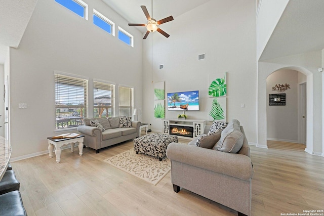 112 La Cima, Boerne, TX 78006 - living room featuring arched walkways, a ceiling fan, light wood-style flooring, a glass covered fireplace, and a high ceiling