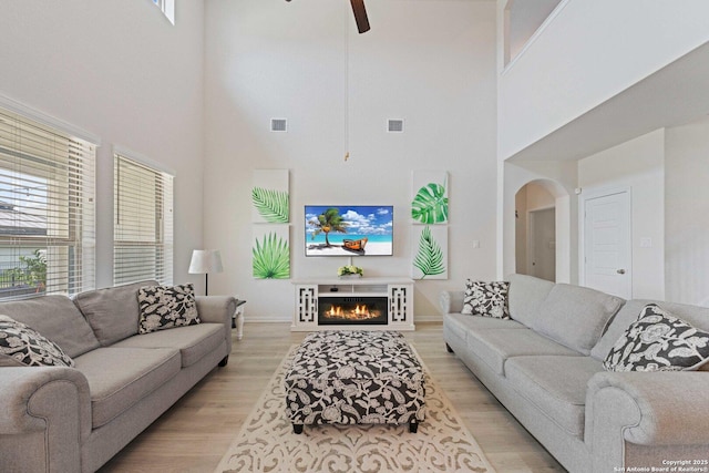 112 La Cima, Boerne, TX 78006 - living room with a high ceiling, a ceiling fan, light wood-style floors, arched walkways, and a lit fireplace