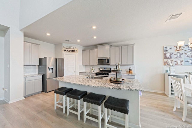 112 La Cima, Boerne, TX 78006 - kitchen with appliances with stainless steel finishes, a sink, gray cabinetry, a center island with sink, and light wood finished floors