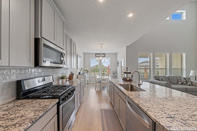 112 La Cima, Boerne, TX 78006 - kitchen with stainless steel appliances, a sink, a chandelier, light wood-style flooring, and light stone countertops