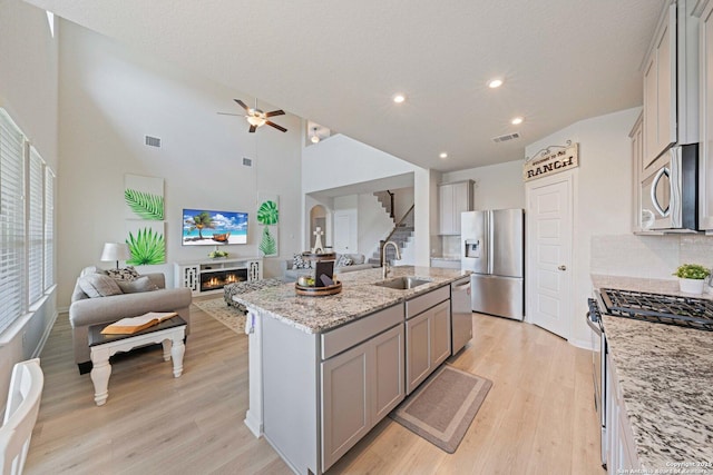 112 La Cima, Boerne, TX 78006 - kitchen with stainless steel appliances, gray cabinetry, a sink, open floor plan, and a lit fireplace