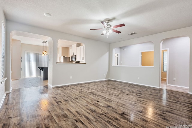 5752 Ping Way, Schertz, TX 78108 - unfurnished living room with dark wood-style floors, a ceiling fan, baseboards, a textured ceiling, and arched walkways
