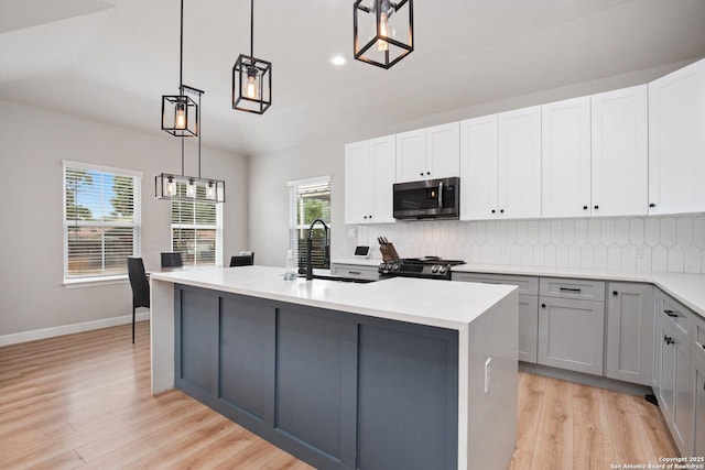 239 Porter, San Antonio, TX 78210 - kitchen with stainless steel microwave, gas stove, light wood finished floors, decorative backsplash, and a center island with sink