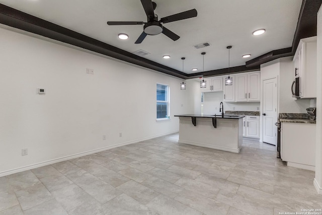 623 Recio St, San Antonio, TX 78225 - kitchen with dark countertops, a ceiling fan, a raised ceiling, a center island with sink, and white cabinetry