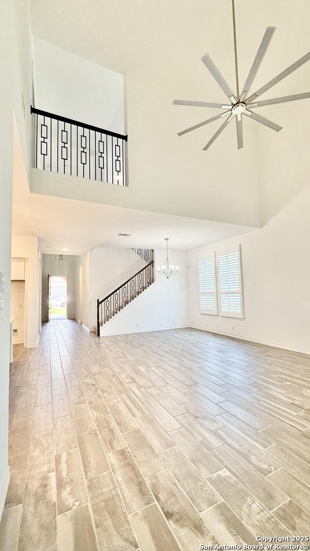 10828 Bango Farms, San Antonio, TX 78254 - unfurnished living room with a towering ceiling, a chandelier, light wood-type flooring, ceiling fan, and baseboards