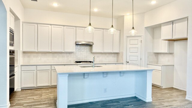 10828 Bango Farms, San Antonio, TX 78254 - kitchen with light wood-style flooring, a center island with sink, decorative backsplash, light countertops, and white cabinetry