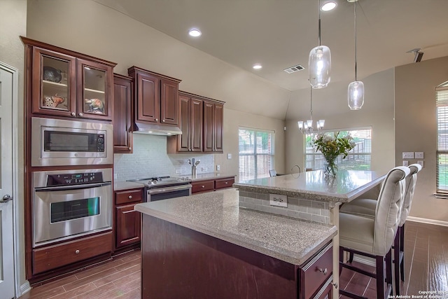 1009 Oak Rdg, Schertz, TX 78154 - kitchen with appliances with stainless steel finishes, under cabinet range hood, a kitchen island with sink, dark wood-style floors, and tasteful backsplash