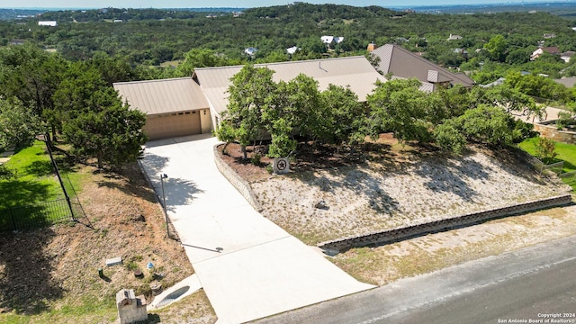 25927 Echo Mtn, San Antonio, TX 78260 - view of front of house with an attached garage, concrete driveway, metal roof, and a forest view