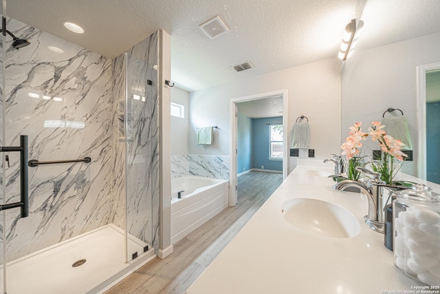 3407 Maguey Trl, San Antonio, TX 78245 - bathroom featuring a bath, a marble finish shower, wood finished floors, double vanity, and a textured ceiling