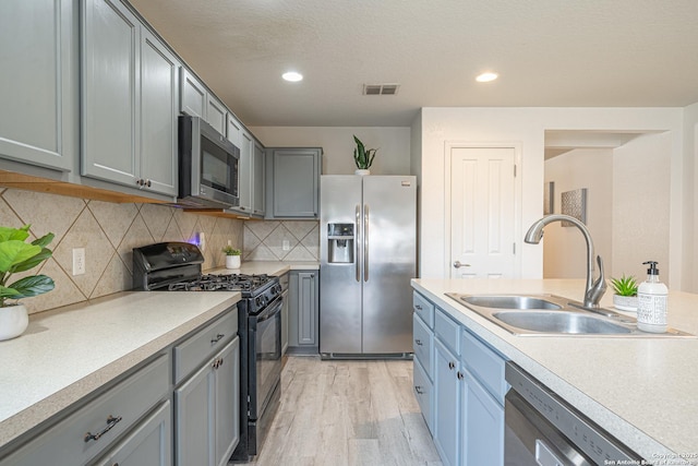 3407 Maguey Trl, San Antonio, TX 78245 - kitchen featuring stainless steel appliances, a sink, light wood finished floors, gray cabinetry, and light countertops